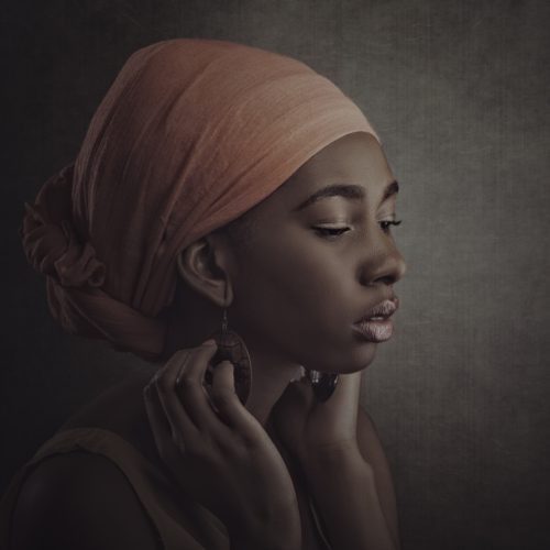Dark skin woman with head wrap looks off camera with hands by her face