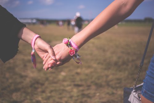 Married & Lonely - Image shows two women's hands grasping each other with flower bracelets