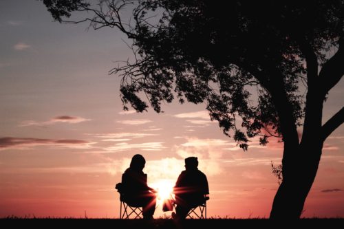 Image shows two people sitting in chairs under a tree at sunset - Listening: A Simple Way to Improve Your Relationship - Alicia Muñoz