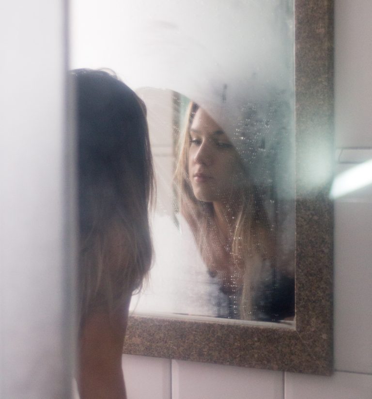 Young woman looking at her reflection in a steamy mirror