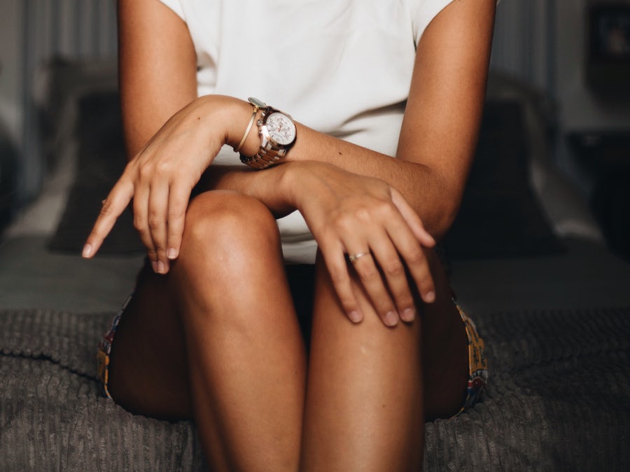 woman from the shoulders down sitting on bed with calves touching and hands crossed and draped over knees