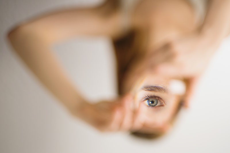 A blurry image of an upside-down woman with one eye reflected right-side up and in focus in the mirror she's holding