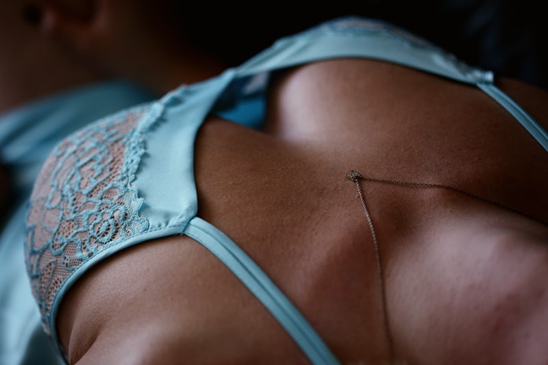 a woman in a blue lingerie with a delicate necklace arches her back in a sensual posture, exposing her neck and cleavage