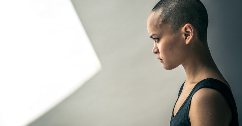 A side-view of a young person in a nondescript white room with close-cropped hair in a sleeveless black shirt staring intently toward the light 