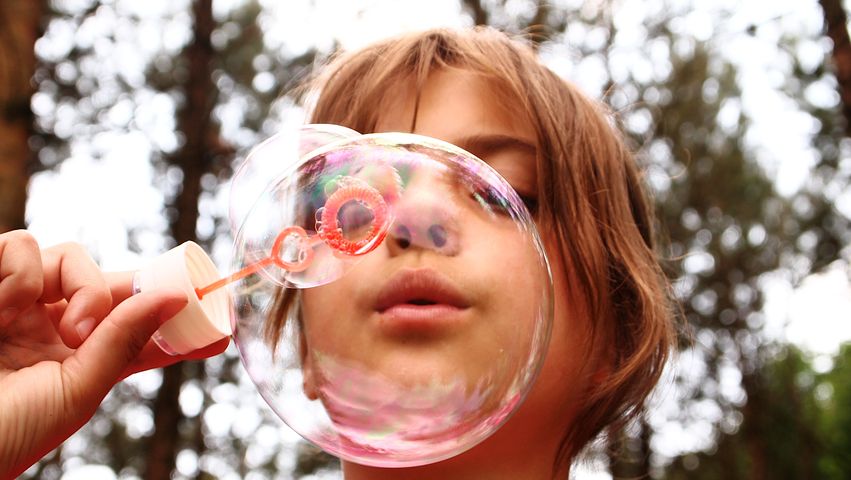 Young girl blowing a bubble against a backdrop of trees.