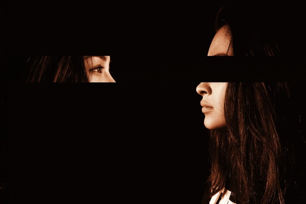 Woman in profile against a dark background with her eyes facing the rest of her face looking at herself.